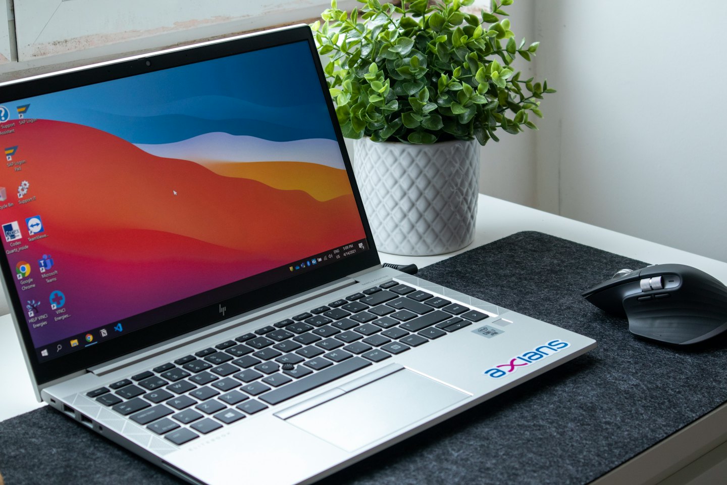 Open laptop with colorful desktop next to a mouse and plant.